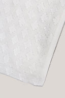 Gros plan sur le coin du tissu Le Coton Indien Tissé 002 écru, détaillant le motif géométrique tissé ton sur ton et la lisière effilochée.