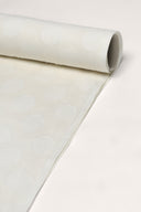 Tissu écru enroulé en rouleau, montrant le motif à pois tissé ton sur ton sur toute la longueur.