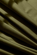 Tissu gabardine légère vert kaki drapé en plis fluides sur l'angle d'un socle blanc.