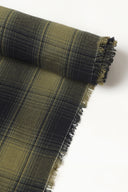 Gros plan sur le coin du tissu Le Carreau 004 kaki et anthracite à carreaux façon tartan ombré, mettant en valeur le motif et la lisière effilochée.