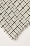 Tissu Le Carreau 011 écru à petits carreaux noir façon quadrillage fin, enroulé en rouleau laissant voir la lisière tissée.