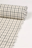 Gros plan sur le coin du tissu Le Carreau 011 écru à petits carreaux noir façon quadrillage fin, mettant en valeur le motif et la lisière effilochée.