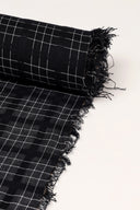 Gros plan sur le coin du tissu Le Carreau 012 anthracite à petits carreaux écru façon quadrillage fin, mettant en valeur le motif et la lisière effilochée.