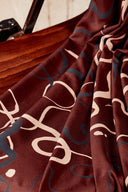 Tissu viscose Misty bordeaux à motif graphique de volutes ivoire, drapé sur l'accoudoir en bois d'une chaise vintage.