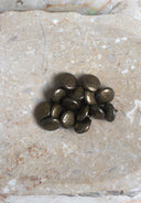Boutons ronds bombés façon galet, finition métallique laiton vieilli patiné brun-doré mat, présentés en tas sur une pierre beige marbrée.