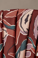 Tissu viscose Peony terracotta à imprimé floral graphique de pivoines écru et sarcelle, drapé sur l'accoudoir en bois d'une chaise vintage.