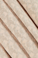 Tissu jacquard rose poudré à motif géométrique pailleté, drapé sur une chaise capitonnée beige.