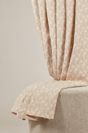 Tissu jacquard rose poudré drapé sur une chaise, avec la lisière effilochée visible en bas.