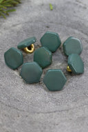 Sept boutons de forme irrégulière façon pierre facettée, coloris vert cactus opaque, avec fixation à queue métallique dorée, posés sur une pierre grise avec un brin de romarin en arrière-plan.