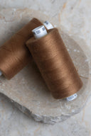 Deux bobines de fil pour surjeteuse Havana Brown marron caramel posées sur une pierre naturelle – Atelier Brunette