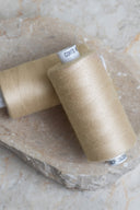 Deux bobines de fil pour surjeteuse Limestone beige sable posées sur une pierre naturelle – Atelier Brunette