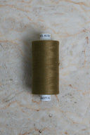 Cône de fil pour surjeteuse Noble Green vert olive posé sur une pierre claire – Atelier Brunette