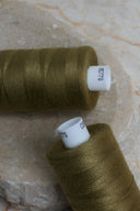 Gros plan sur deux bobines de fil pour surjeteuse Noble Green et leur étiquette de référence – Atelier Brunette