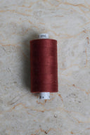 Cône de fil pour surjeteuse Velvet Syrah rouge bordeaux posé sur une pierre claire – Atelier Brunette