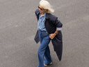 Femme aux cheveux blancs en trench bleu marine, chemise en jean et jean large, marchant dans la rue – Patron Le Trench Atelier Brunette