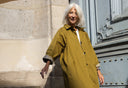 Femme aux cheveux blancs en manteau long kaki à poignets à carreaux, devant une porte parisienne – Meilleures ventes Atelier Brunette