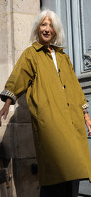 Femme aux cheveux blancs en manteau long kaki à poignets à carreaux, devant une porte parisienne, cadrage vertical – Meilleures ventes Atelier Brunette