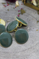 Mêmes boutons Gem vert cèdre facettés, gros plan sous un angle différent laissant voir l'anneau de couture doré à l'arrière d'un bouton.