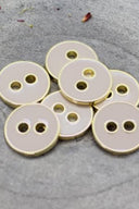 Cinq boutons ronds à deux trous, finition émaillée brillante rose pâle blush, cerclés d'un liseré métallique doré, posés sur une pierre grise avec des pétales de fleurs séchées éparpillés en arrière-plan.