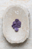 Boutons ronds bombés à queue, sans trous apparents, finition nacrée violet parme, présentés en tas de tailles variées dans une coupelle en pierre ovale beige marbrée.