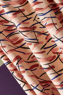Fuji fabric in powder pink with graphic strokes in terracotta, black and navy blue, draped over a white stand near a decorative ornamental onion flower.