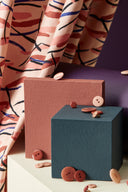 Fuji fabric in powder pink folded among colored stands (terracotta, anthracite), with a small dish of pink and terracotta buttons.
