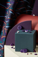 Fuji fabric in anthracite folded among colored stands, with a small dish of matching plum buttons.