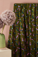 Java fabric in khaki draped over a white stand and a pink side table, with a ceramic vase and a decorative ornamental onion flower.