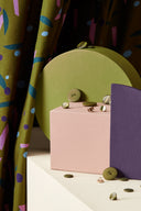 Java fabric in khaki folded among colored stands (olive green, powder pink, plum) with khaki and gold buttons scattered around.