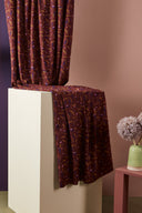 Gros plan sur les plis satinés du tissu Java bordeaux à motif confettis rose, moutarde et prune.
