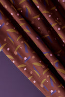 Tissu Java bordeaux plié parmi des socles colorés (terracotta, anthracite) avec des boutons rouille et prune dispersés.