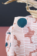 Close-up of the Mirage fabric in off-white, showing navy polka dots and terracotta spots on a striped background, with a dried leaf in the background.