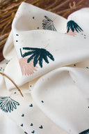 Palmetto fabric in ivory with a stylized palm-leaf pattern in navy and powder pink, folded on a wooden stand in front of a terracotta background.