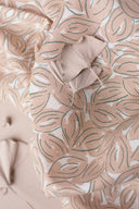 Tissu Petal écru à motif de feuilles graphiques terracotta et sauge, plié avec une feuille de ginkgo séchée posée dessus.