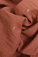 Close-up of the Sunset cotton gauze in terracotta, showing the golden sun-shaped embroidery.