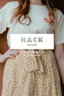 Hack La Jupe – Femme torse, jupe léopard camel taille haute ceinture nouée, t-shirt écru, fond marron – Atelier Brunette