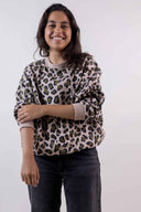 Patron Le Hoodie – Femme de face souriante, sweat oversize léopard beige et vert, bras croisés, fond gris – Atelier Brunette