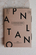 Patron Le Pantalon Short – Étui patron kraft avec nom de la collection imprimé, posé contre mur texturé – Atelier Brunette