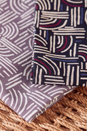Tissus Hopscotch pliés dans deux coloris, mauve et marine, posés sur un support en raphia tressé.
