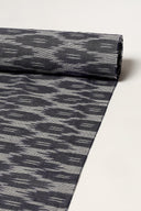 Anthracite cotton voile rolled up, showing the abstract ikat-style pattern along its full length.