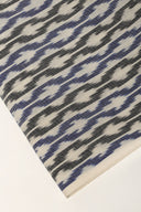 Close-up of the folded corner of the off-white fabric, showing the blue and anthracite ikat-style chevrons and the off-white selvedge.