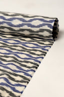 Off-white fabric rolled up, showing the blue and anthracite ikat-style chevron pattern along its full length.