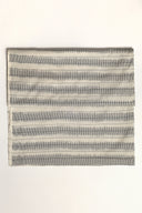 L'Ikat fabric in off-white folded flat, with anthracite ikat-style stripes arranged in regular bands across the whole piece.