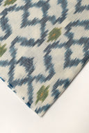 Close-up of the folded corner of the off-white fabric, showing the indigo blue ikat-style diamonds and the frayed selvedge.
