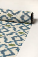 Off-white fabric rolled up, showing the indigo blue ikat-style diamond pattern along its full length.
