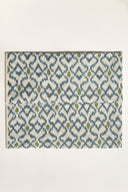 L'Ikat fabric in off-white folded flat, with an indigo blue diamond trellis pattern accented with olive green and orange touches.