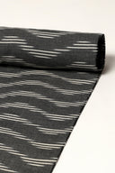 Anthracite fabric rolled up, showing the diagonal off-white ikat-style stripes along its full length.