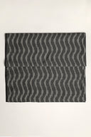 L'Ikat fabric in anthracite folded flat, with a wavy off-white ikat-style stripe pattern forming a diamond design across the whole piece.