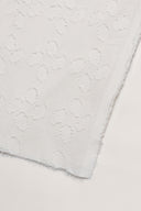 Close-up of the corner of the Le Coton Indien Tissé 001 ecru fabric, detailing the tone-on-tone woven floral pattern and the frayed selvedge.
