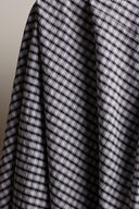 Gros plan sur les carreaux vichy anthracite et écru du tissu seersucker, mettant en valeur le grain irrégulier de la texture gaufrée.